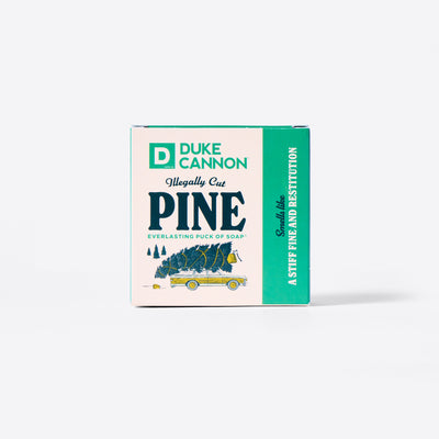 The back of the Duke Cannon Illegally Cut Pine Everlasting Puck of Soap packaging with the Soap Puck on the inside. On a white background. Says, "Smells like a stiff fine and restitution."