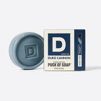 Puck shaped Bar of soap with Duke Cannon packaging on a white Background. Midnight Swim and Sandalwood + Lavender scent.