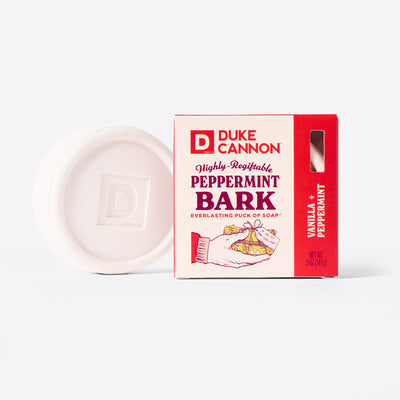 Duke Cannon Highly Regiftable Peppermint Bark Everlasting Puck of Soap next to it's packaging. On a white background. The soap puck itself is white. Scent is Vanilla + Peppermint. 