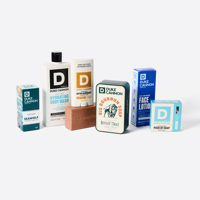Collection of Duke Cannon products including body wash, soap, and lotions on a white background. Products seen: Seawolf Proper Cologne, Hydrating Body Wash, Sawtooth Aluminum Free Deodorant, Bourbon Big Ass Brick with Tin. Face Lotion and Midway Puck of Soap.